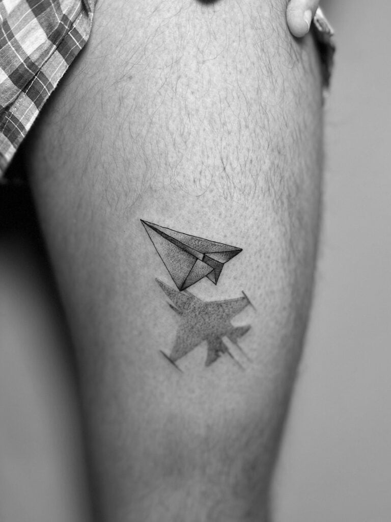 Tatuaje de avión de papel con sombra en muslo