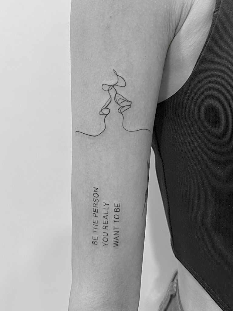 Tatuaje de línea fina de silueta de caras y frase en el brazo