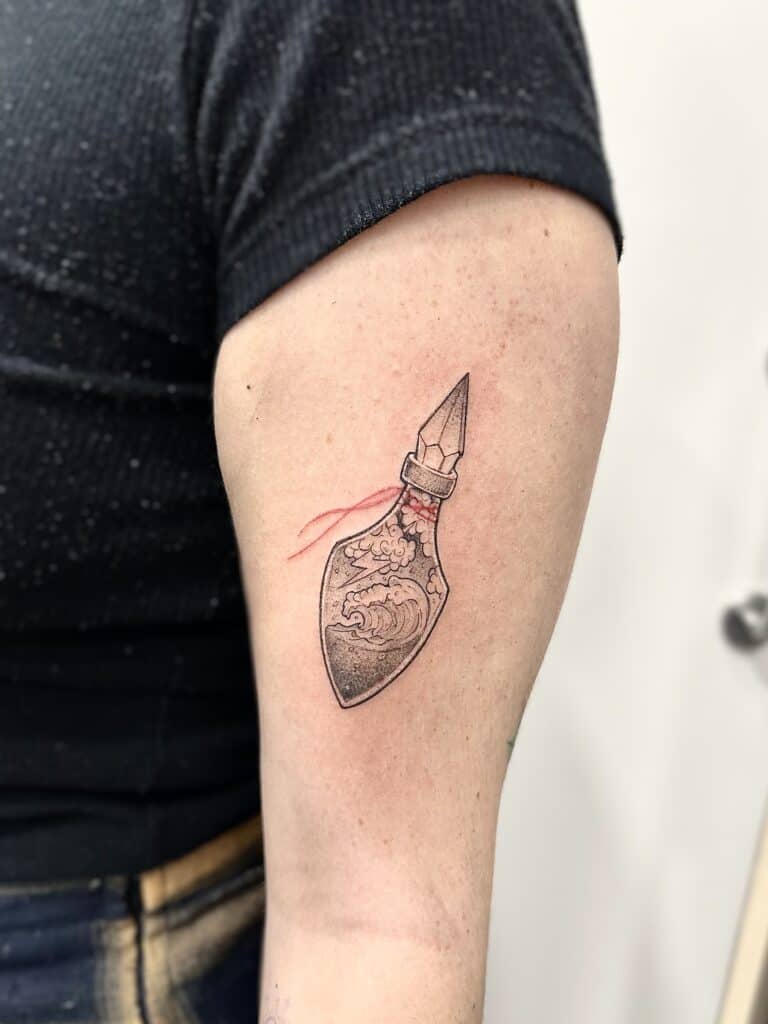 Tatuaje de línea fina de botella con detalla en rojo en el brazo