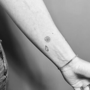 Tatuaje de línea fina mini caracolas en antebrazo