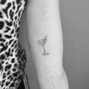 Tatuaje de copa de coctel en línea fina en el brazo