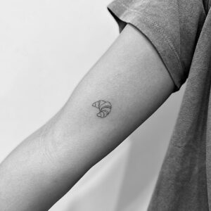 Tatuaje de mini cruasan de línea fina en brazo