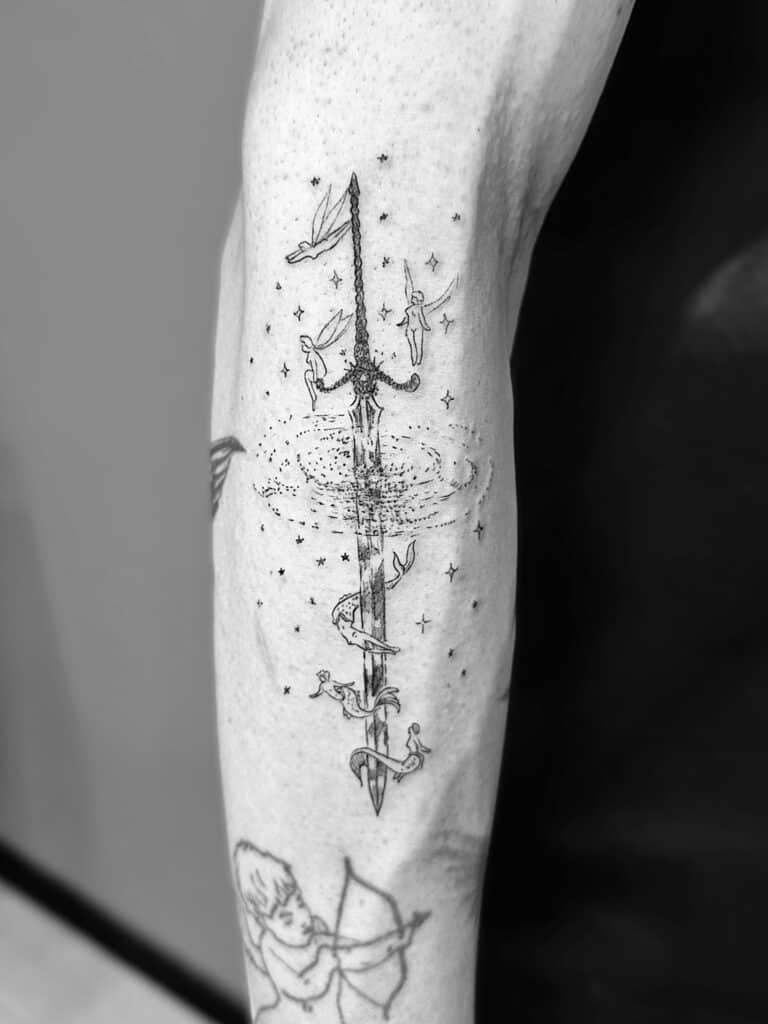 Tatuaje de línea fina de espada de fantasía en el antebrazo