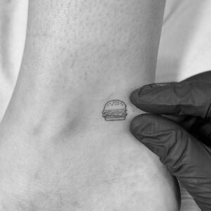 Tatuaje línea fina de mini hamburguesa en el tobillo