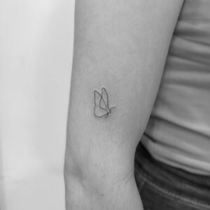Tatuaje línea fina de mariposa minimalista en el brazo