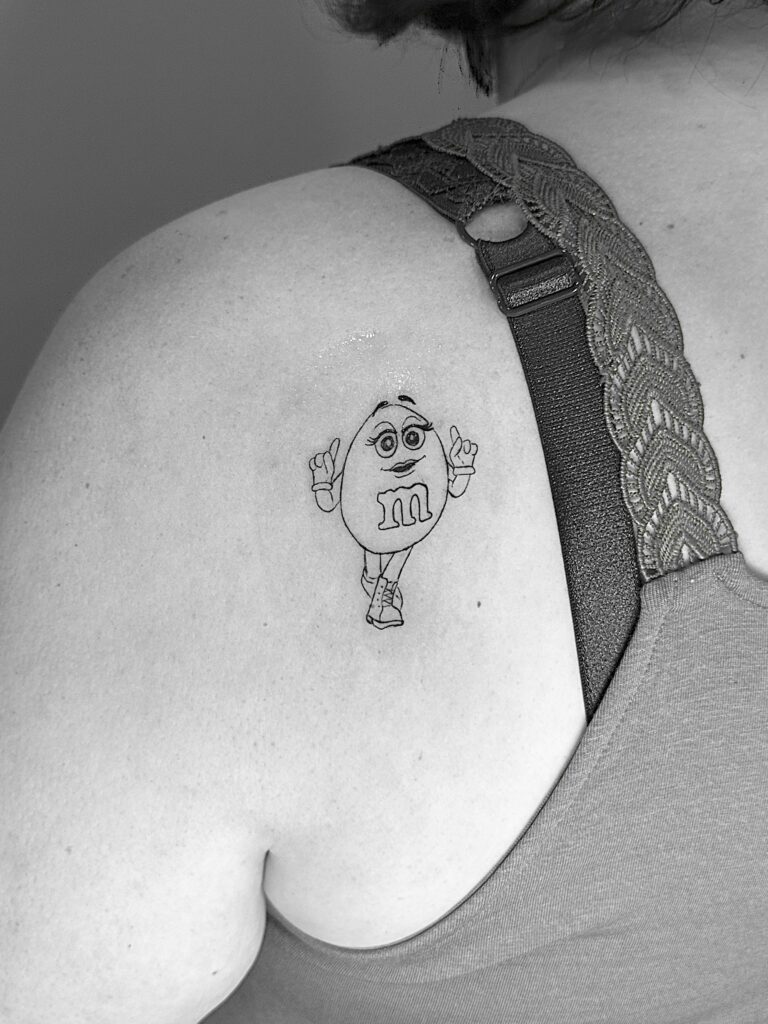 Tatuaje de línea fina de un M&M femenino en el hombro