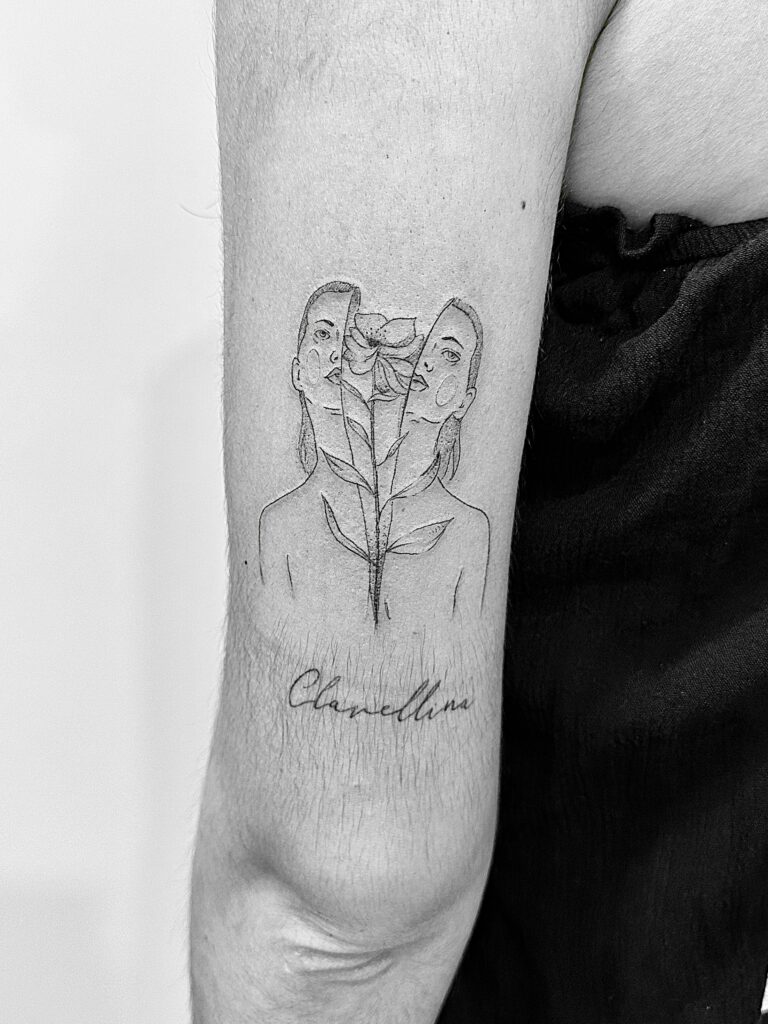 Tatuaje de línea fina de mujer partida en dos con flor en el brazo