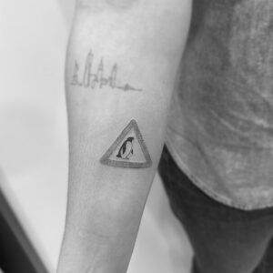 Tatuaje pequeño de señal pingüino en antebrazo