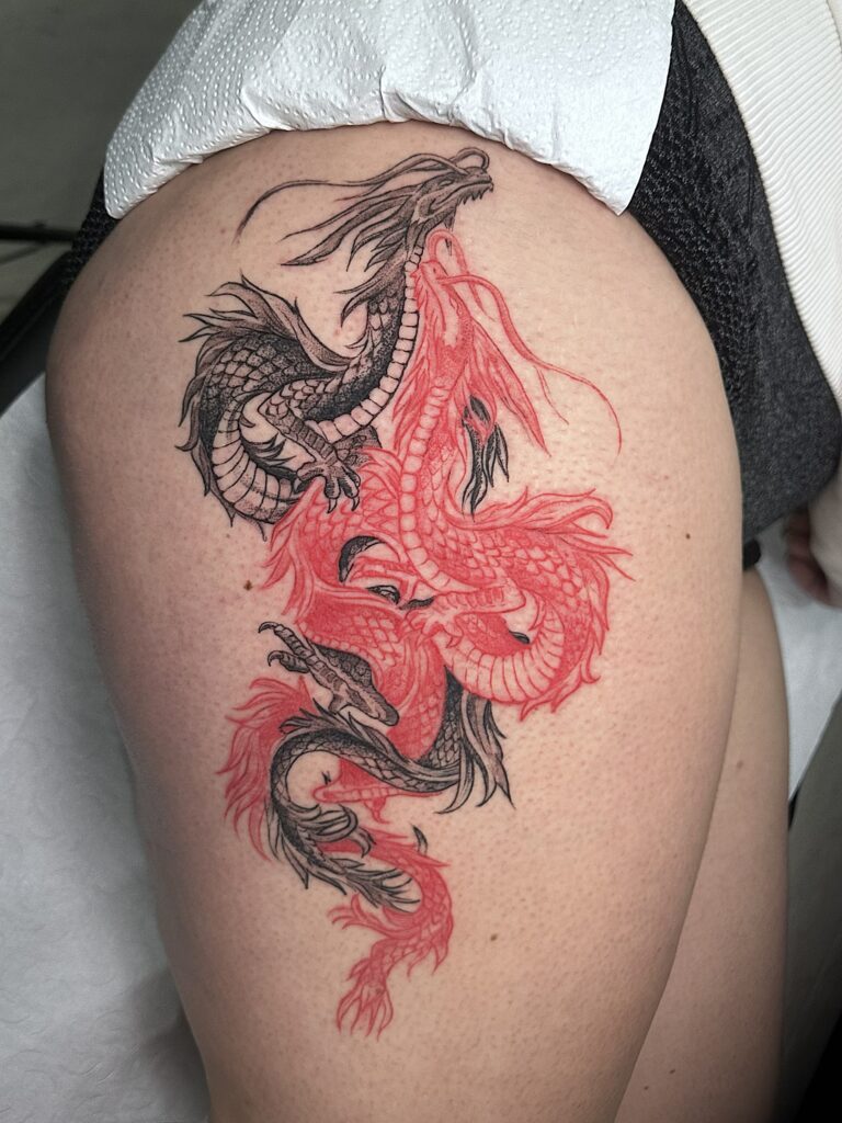 Dos dragones entrelazados, uno rojo, en el muslo