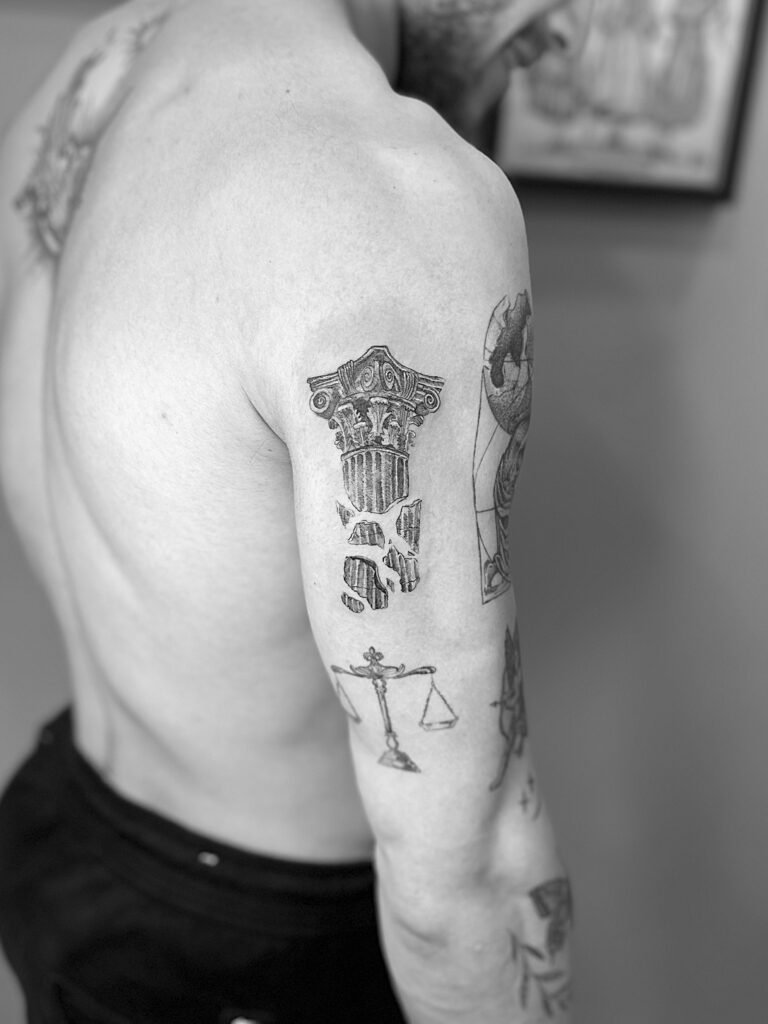 Tatuaje en línea fina de una columna griega rota en el brazo