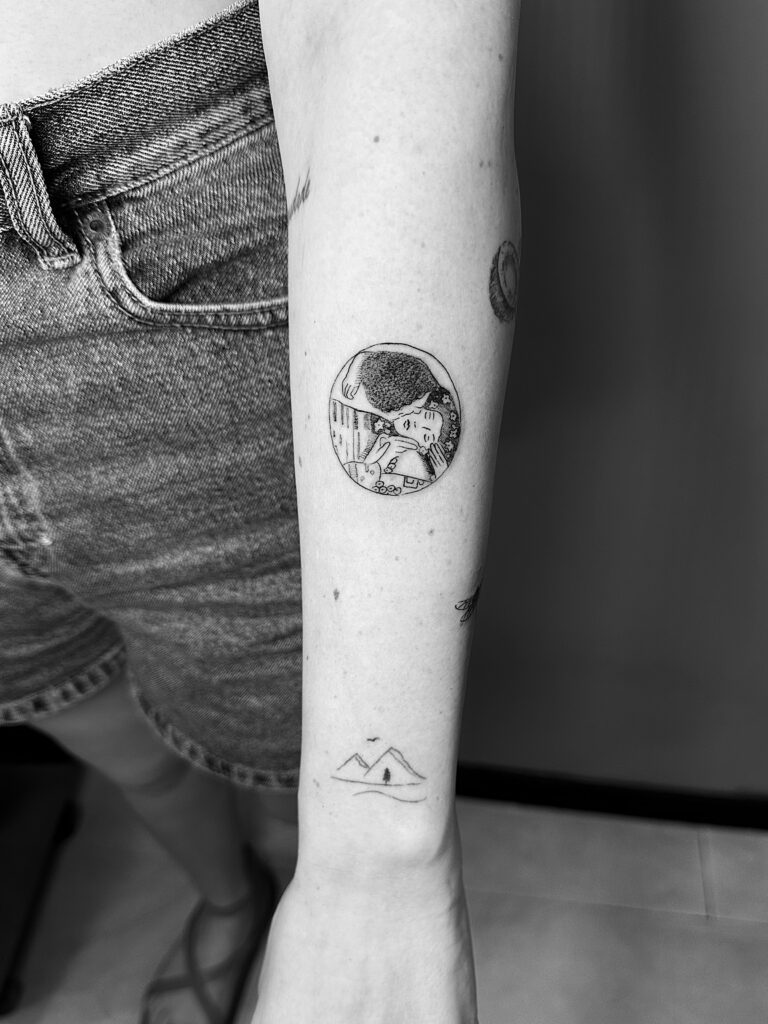 Tatuaje en línea fina de la pintura de El Beso de Klimt en forma circular en el antebrazo