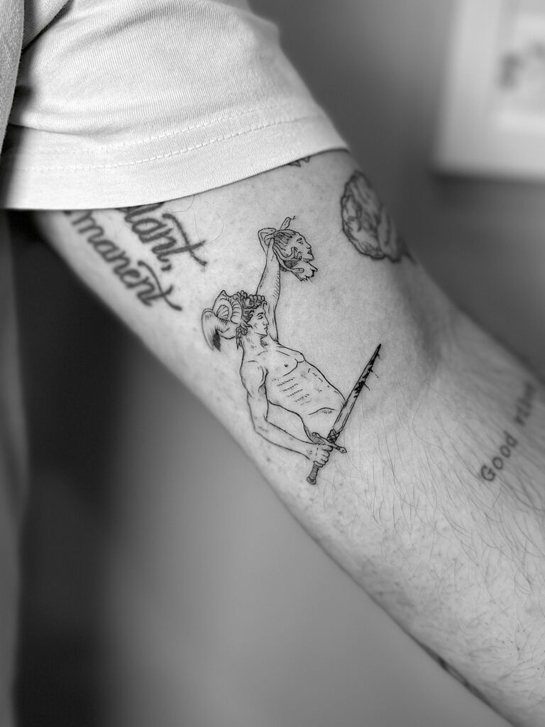 Tatuaje en línea fina de Hércules cortando la cabeza de Medusa en el brazo
